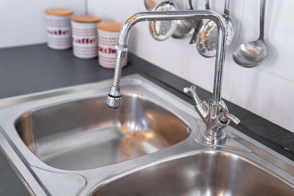 Un évier de cuisine en acier inoxydable, doté d’un robinet moderne, d’un plan de travail noir et d’un dosseret de carrelage blanc.