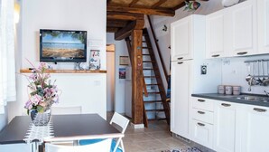 A kitchen with white cabinets, a wooden ceiling, a TV mounted on the wall, and a staircase leading to another level. - Cozy Beachfront House with Stunning Sea View | Mandriola - Putzu Idu (Mandriola)