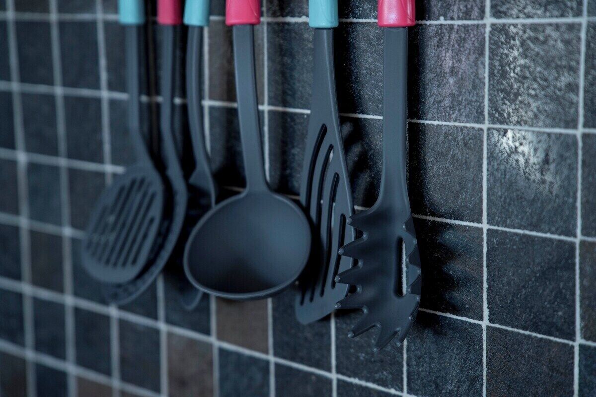 A kitchen backsplash with black tiles and a few kitchen utensils hanging on the wall.