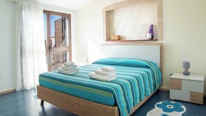 Ein Schlafzimmer mit einem Bett, einem Nachttisch, einem Fenster mit Vorhängen und einem an der Wand befestigten Regal mit Dekoration.