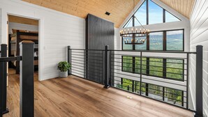 A spacious balcony with wooden flooring, a black metal railing, and a view of a green landscape through large windows. - MtnTopRetreat: MtnView*Pool*Theater*Games*HotTub*WiFi*Fireplaces*ResortPool (Gatlinburg)