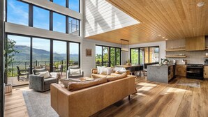 A spacious living area with a large sofa, a dining table, and a kitchen area with wooden flooring and large windows offering a mountain view. - MtnTopRetreat: MtnView*Pool*Theater*Games*HotTub*WiFi*Fireplaces*ResortPool (Gatlinburg)