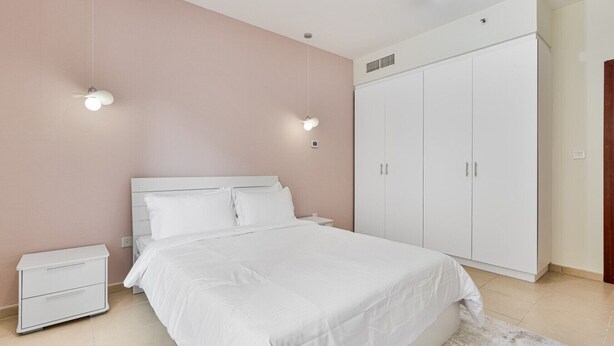 A bedroom with a bed, nightstand, wardrobe, and pendant lights. - Savis Home – Oceanfront Serenity & Marina Views (Dubai)