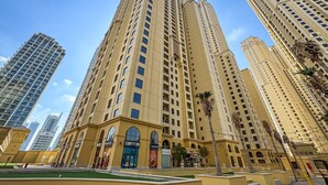 A high-rise building with multiple floors, large windows, and a prominent entrance with arches. - Savis Home – Oceanfront Serenity & Marina Views (Dubai)