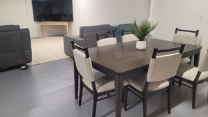 Ein modernes Wohnzimmer mit einem dunklen Esstisch, sechs gepolsterten Stühlen, einem flachbildfernseher an der Wand und einem Blumentopf auf dem Tisch.