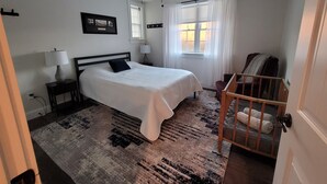 Ein Schlafzimmer mit einem Bett, einem Deckenventilator, einem Fenster mit Vorhängen, einem Sessel und einem Teppich.