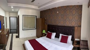 Habitación de hotel con una cama grande, televisión, escritorio y baño al fondo.