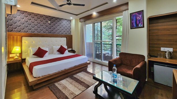Habitación de hotel con cama, ventilador de techo, ventana con vistas, mesa de centro y un refrigerador pequeño.