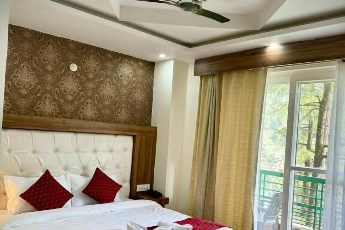 Une chambre d’hôtel avec un grand lit, un ventilateur de plafond et une vue sur la verdure par la fenêtre.
