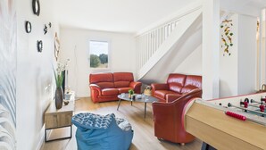 Een moderne woonkamer met een rode leren bank, een blauwe kruikzak en een tafelvoetbaltafel.