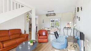 Een moderne woonkamer met een bruine leren bank, een blauwe relaxfauteuil, een klein rond tafeltje met glazen en een tafelvoetbal.
