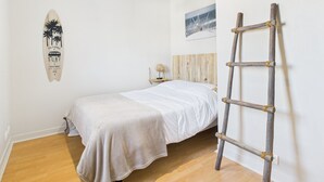 Een slaapkamer met een bed, een hangende lamp, een houten ladder, een surfboard als decoratie, en een schilderij aan de muur.