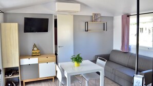 A compact living space with a sofa, a dining table with chairs, a TV mounted on the wall, a small cabinet, and a potted plant. - Chalet for 6 in St-Hilaire - Heated swimming pool (Saint-Hilaire-de-Riez)