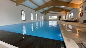 An indoor swimming pool with a blue water surface, wooden beams on the ceiling, and a lifebuoy on the wall. - Chalet for 6 in St-Hilaire - Heated swimming pool (Saint-Hilaire-de-Riez)
