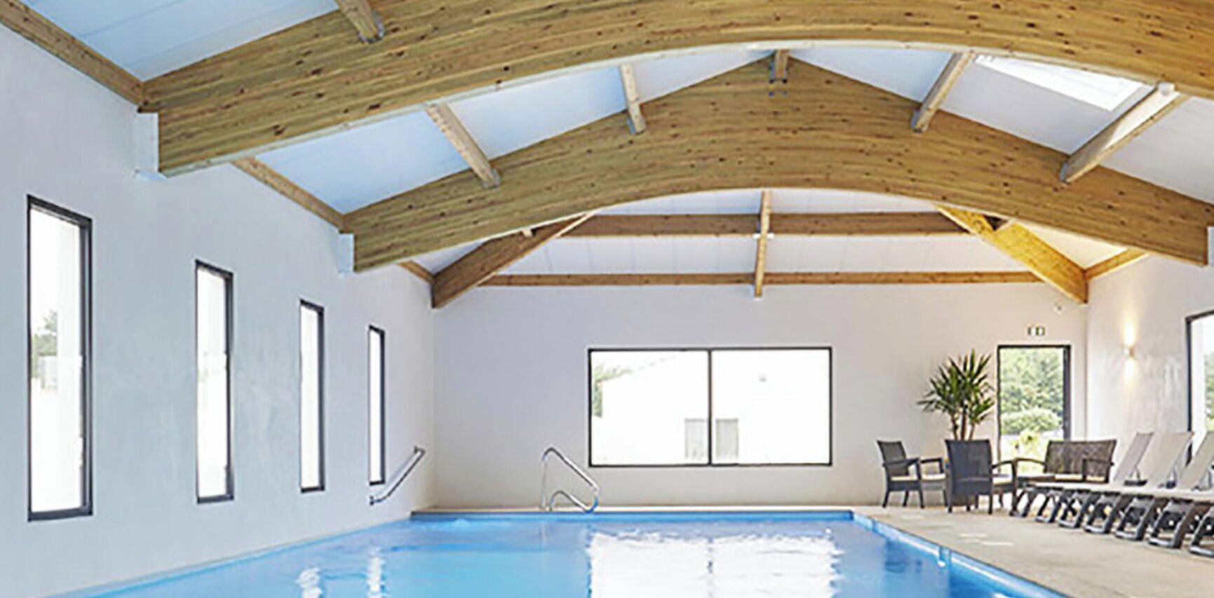 An indoor swimming pool with a high wooden ceiling and large windows.