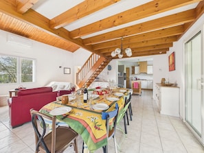 A dining area with a wooden ceiling, a staircase, a kitchen, and a living room with a red sofa.