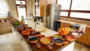 A kitchen with a central island filled with various bowls and containers, a stainless steel refrigerator, and a window providing natural light. - Glory Art Stone House (Nevsehir)