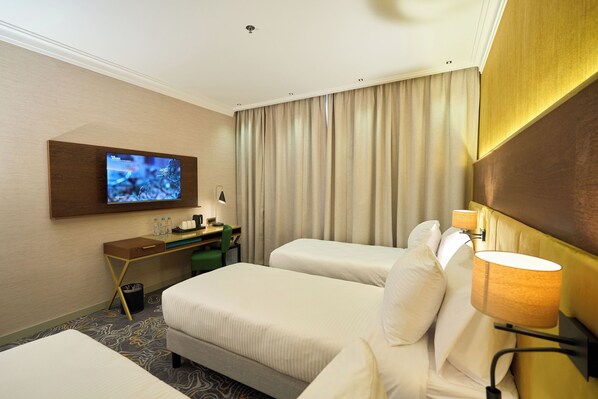A hotel room with two beds, a desk with a computer, a TV mounted on the wall, and a curtain.