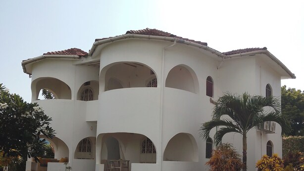 A multi-story building with a white facade and red-tiled roof. It features multiple balconies and arched windows. - Four shells apartments diani  (Diani Beach)