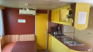 Una kitchenette compacta con estufa, pileta y armarios amarillos. Se observa un banco a rayas y una puerta que da a otra habitación.