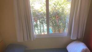 Una habitación pequeña con una cama individual, una ventana con cortinas y vistas a árboles.
