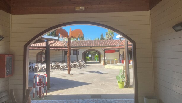 Una entrada arqueada a un edificio con techo de tejas, área de estar al aire libre y una planta de cactus.
