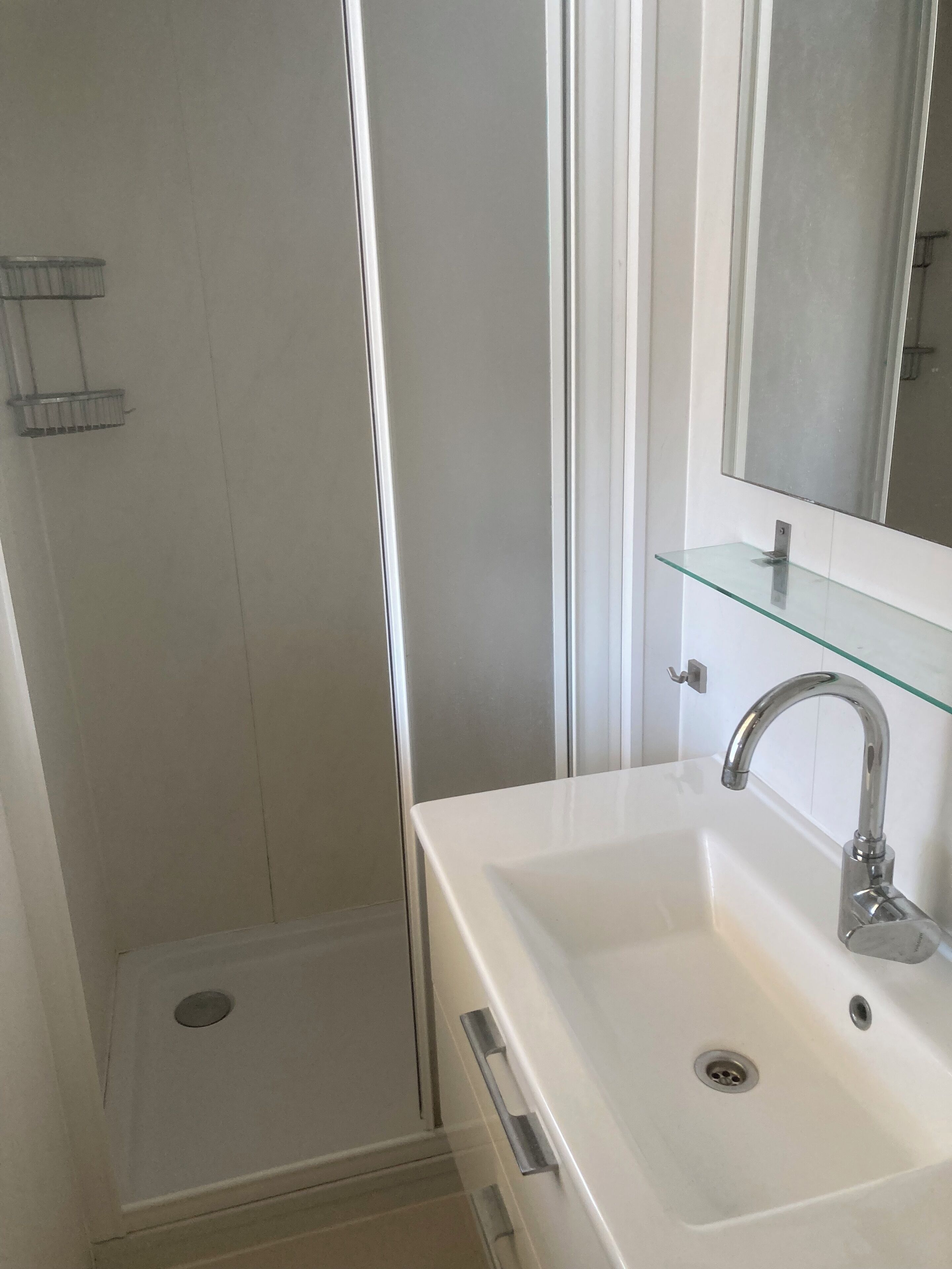 A bathroom with a white sink, a glass shelf, a mirror, and a shower area.