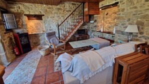 A cozy room with a stone wall, wooden ceiling, a sofa, a table, a chair, a fireplace, and a staircase.