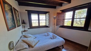 A bedroom with a bed, two windows, a lamp, and a wall-mounted heater.