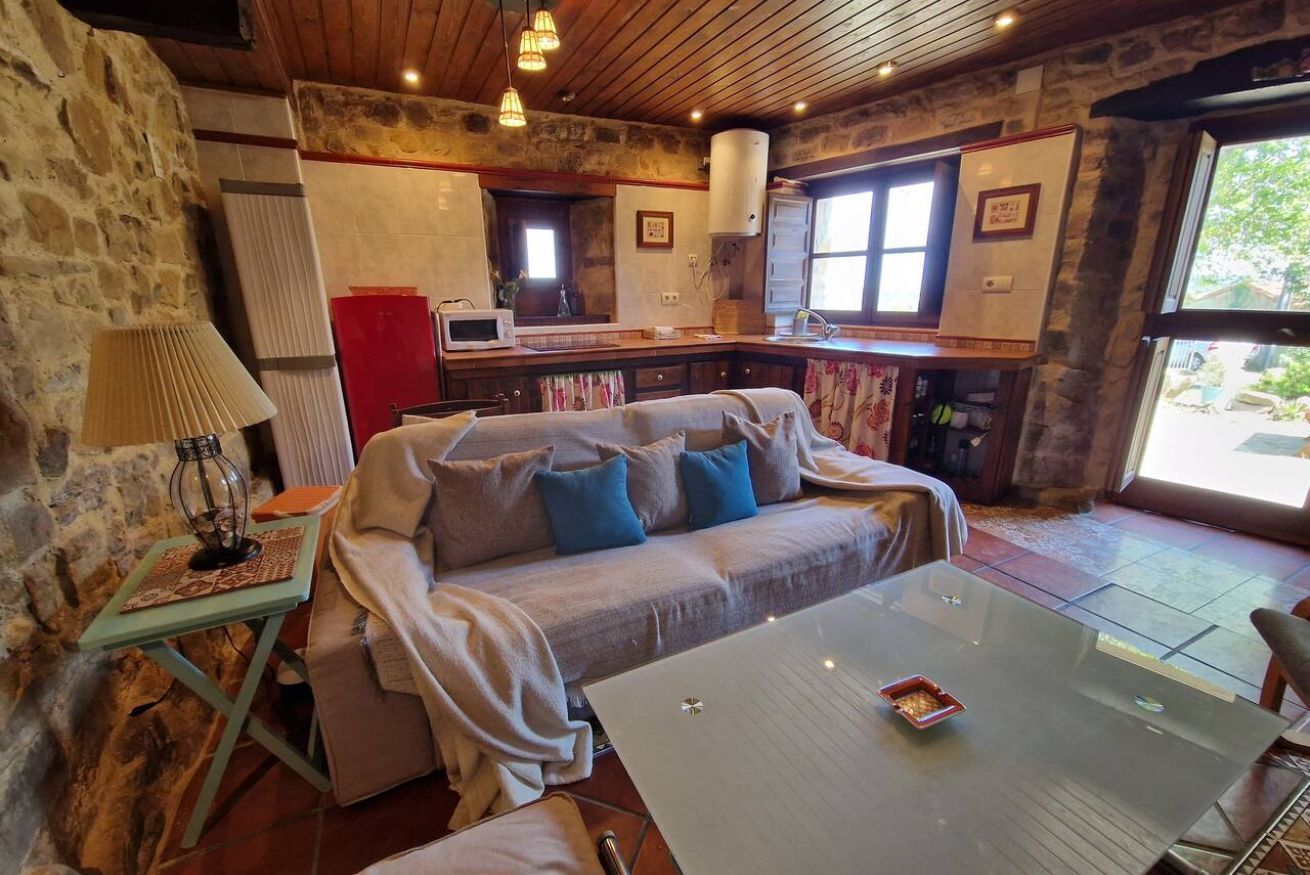 Una habitació acollidora amb un sofà, una taula de vidre, una làmpada i una zona de cuina amb microones.