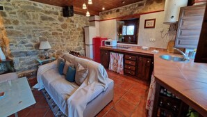 A cozy living room with a sofa, a small table, a kitchen area with a microwave, and a stone wall.