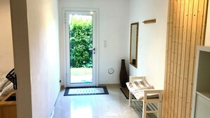 A hallway with a white door leading to a garden, a white bench, a mirror, and a wooden wall. - Beautiful apartment with garden seating area in Rapperswil-Jona (Rapperswil-Jona)