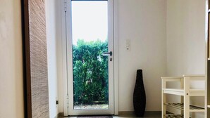A hallway with a glass door leading to a garden, a black vase, and a white shelf unit. - Beautiful apartment with garden seating area in Rapperswil-Jona (Rapperswil-Jona)