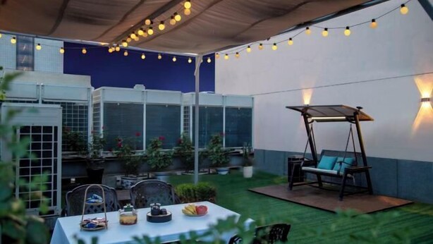 Une terrasse extérieure agrémentée de guirlandes lumineuses, d’une balançoire et d’une table sur laquelle sont disposés des fruits et une théière.
