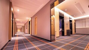 A hotel corridor with a checkered carpet, doors, and a window with curtains.