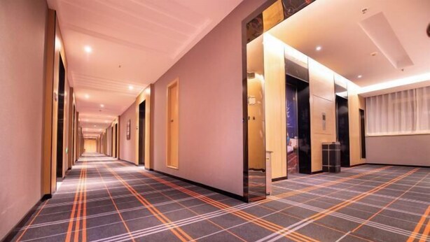 Un couloir d’hôtel avec un tapis à carreaux, des portes et une fenêtre avec des rideaux.
