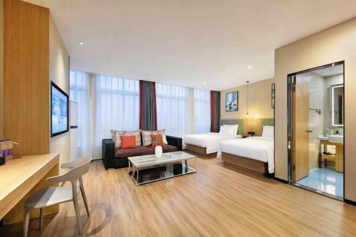 Una habitación de hotel con piso de madera, un sofá, una cama, un escritorio y un espejo.