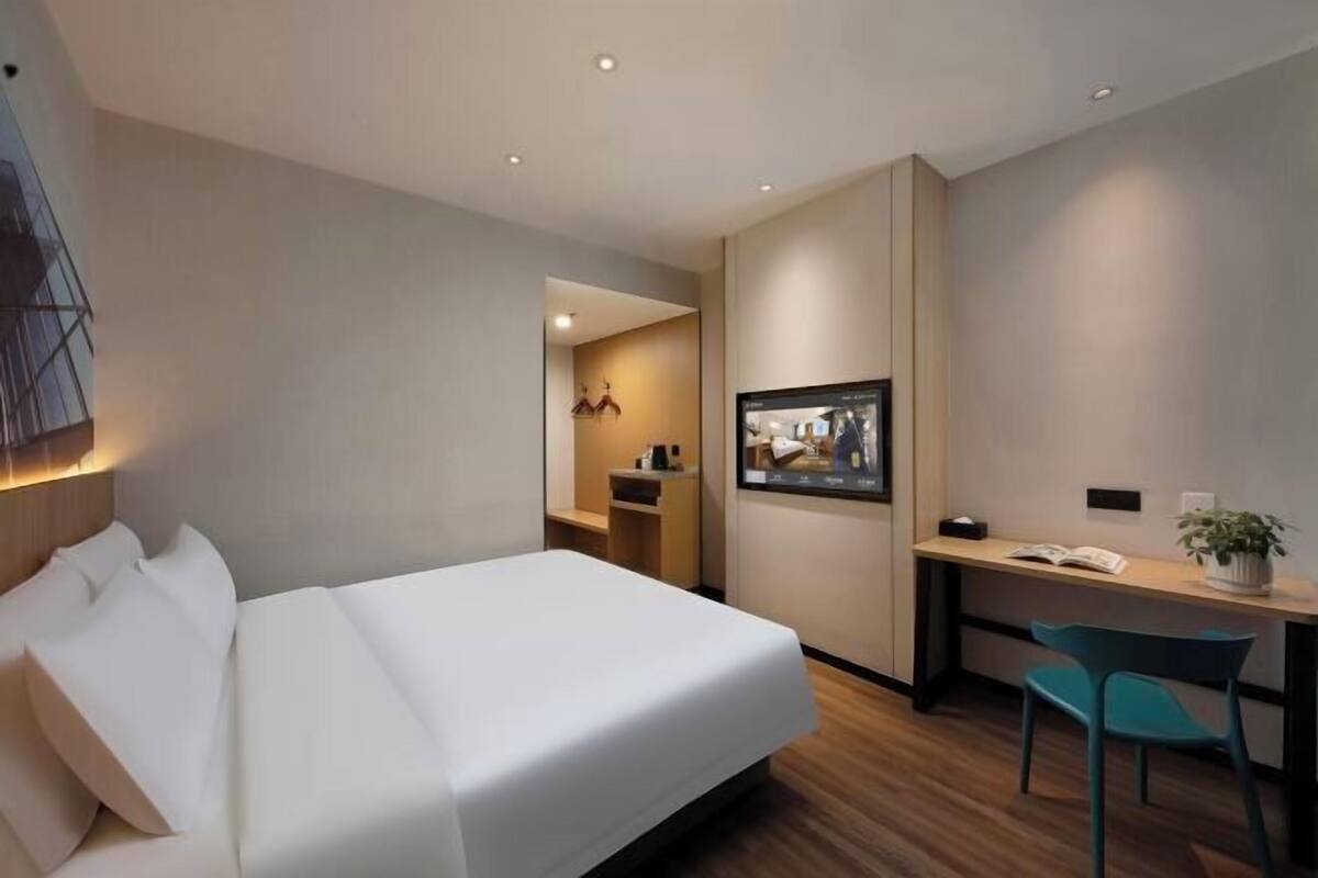 Habitación de hotel con cama, escritorio, silla, televisor y un pequeño rincón de descanso.