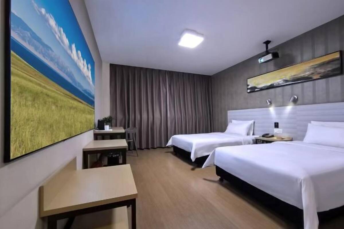 Habitación de hotel con dos camas, un escritorio, una silla y un cuadro grande de un paisaje.