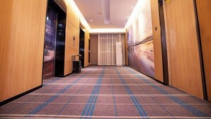 A hotel hallway with wooden walls, a patterned carpet, and a large window with a view of a cityscape.