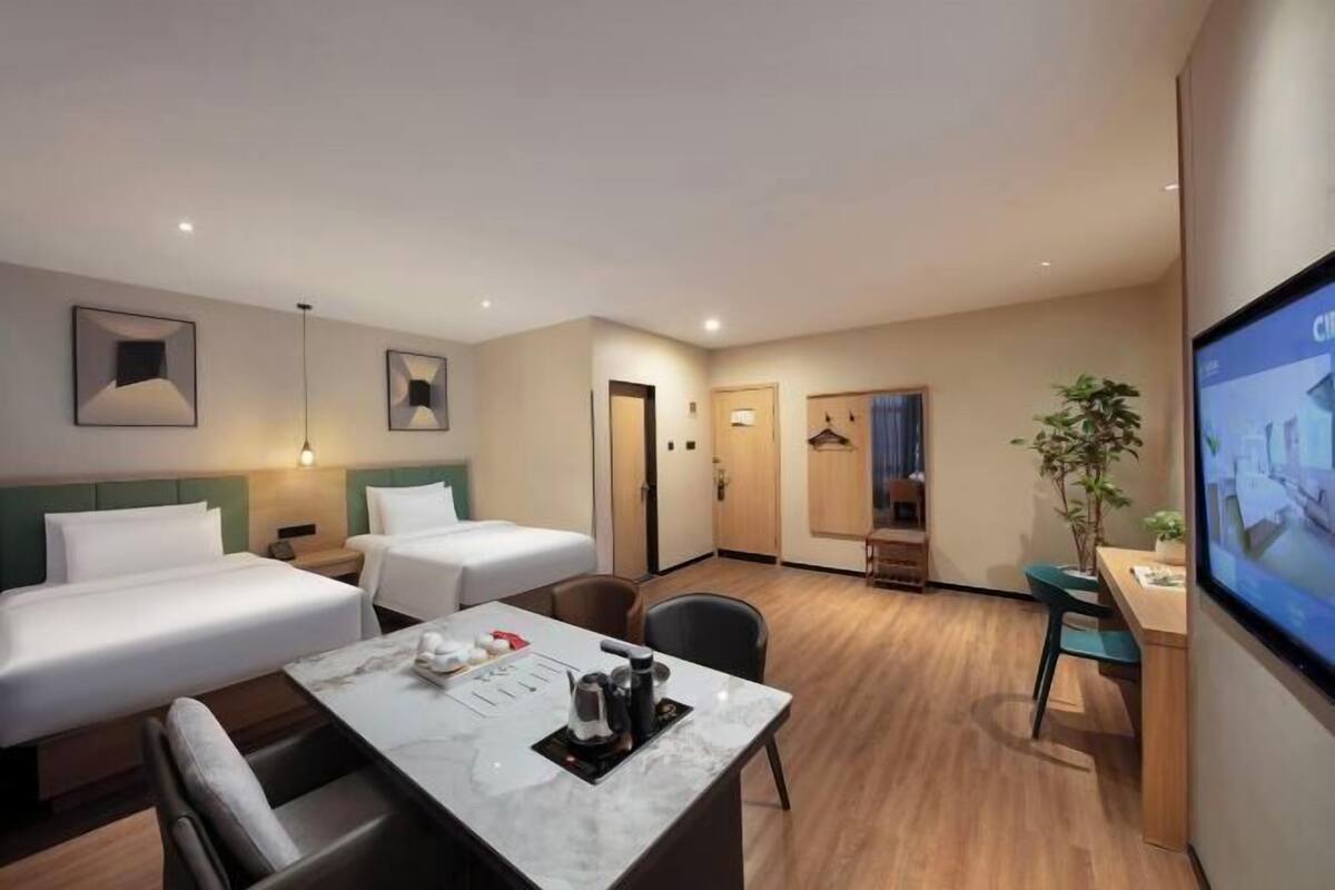 Habitación de hotel con dos camas, una mesa de comedor con sillas, un televisor y un escritorio.