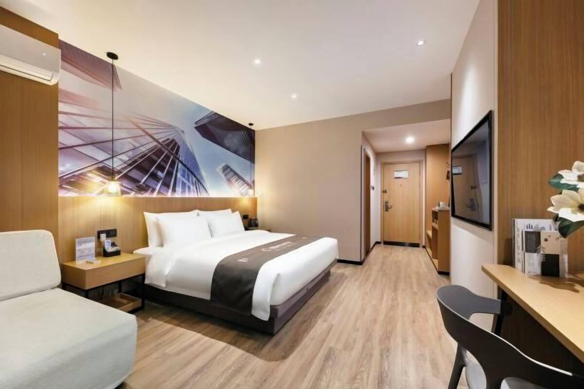 Una habitación de hotel con cama, mesita de noche, escritorio, silla y un mural grande en la pared.