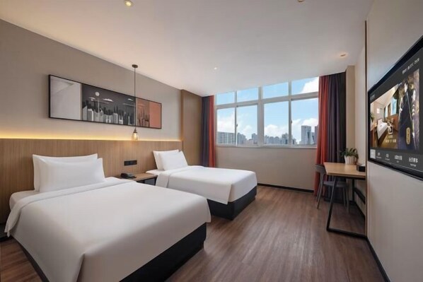 Quarto de hotel com duas camas, uma escrivaninha, uma cadeira, uma janela com vista para a cidade e um quadro na parede.