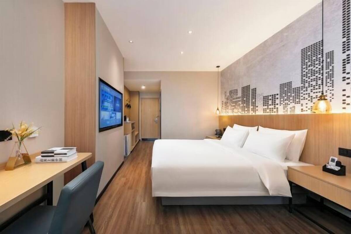 Una habitación de hotel moderna con una cama grande, un escritorio y un mural con un paisaje urbano en la pared.