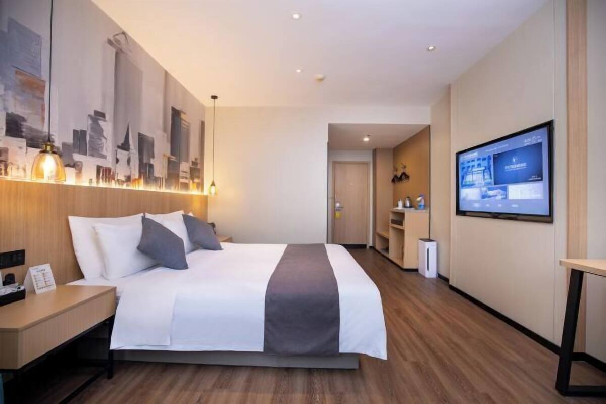Habitación de hotel con cama, mesita de noche, decoración en la pared, televisor y puerta que da a un baño.