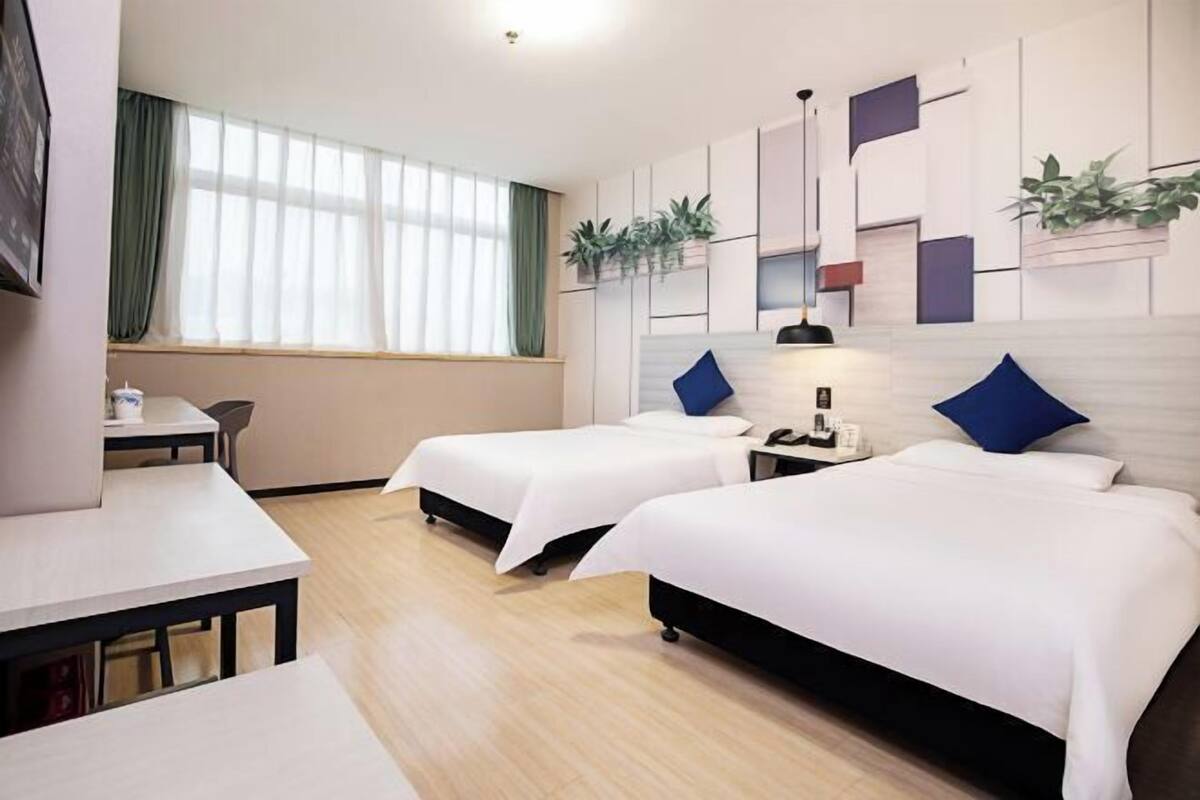 Habitación de hotel con dos camas, un escritorio y una ventana con cortinas.