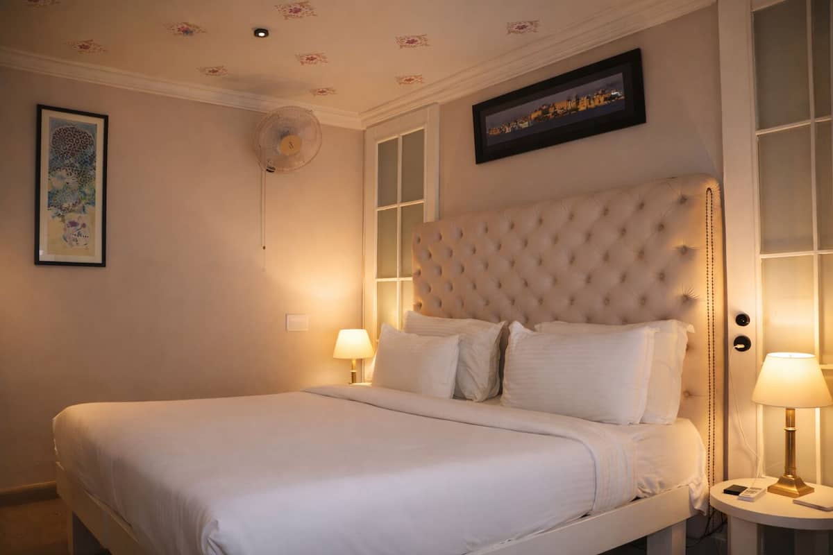 Un cuarto de hotel con una cama grande, dos lámparas de noche, un ventilador de techo y un cuadro enmarcado en la pared.