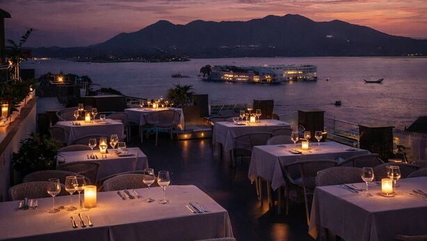 Un restaurant amb vistes al mar, amb taules preparades per dinar, davant una calma extensió d'aigua i muntanyes allunyades.