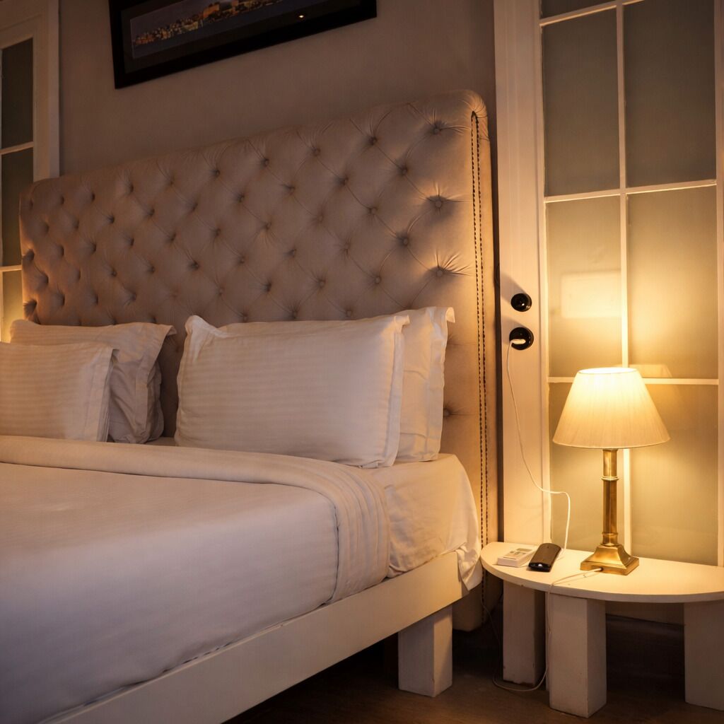 Un lit doté d’une tête de lit capitonnée, de draps blancs et d’une table de chevet avec une lampe et un téléphone.