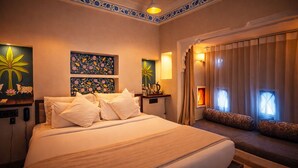 Habitació d'hotel amb un llit gran, una taula de nit amb una làmpada, una paret decorativa amb motius florals i una finestra amb cortines.